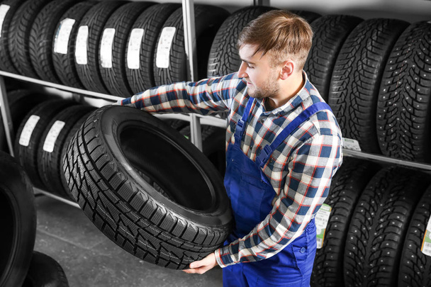 Jeune mécanicien masculin avec pneu de voiture dans le centre de service automobile
 - Photo, image