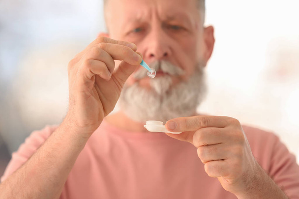 Senior man taking contact lens from container on blurred background - Φωτογραφία, εικόνα
