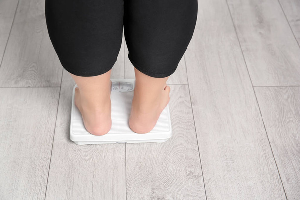 Mulher com excesso de peso usando escalas dentro de casa
 - Foto, Imagem