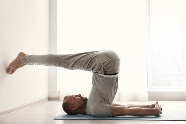 Sporty man practicing yoga indoors - Фото, изображение