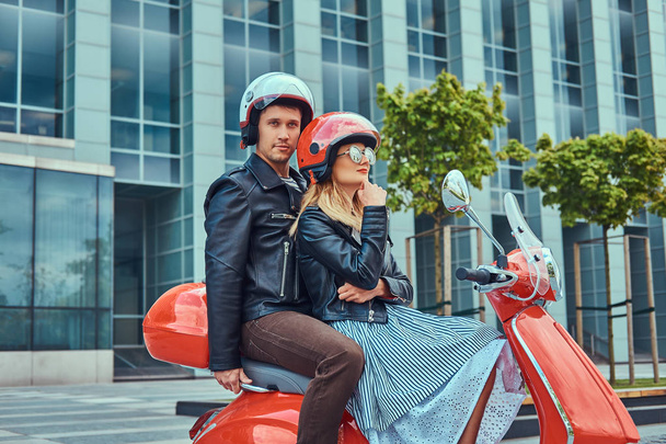 Coppia attraente, un bell'uomo e una donna sexy che cavalcano insieme su uno scooter rosso retrò in una città
. - Foto, immagini