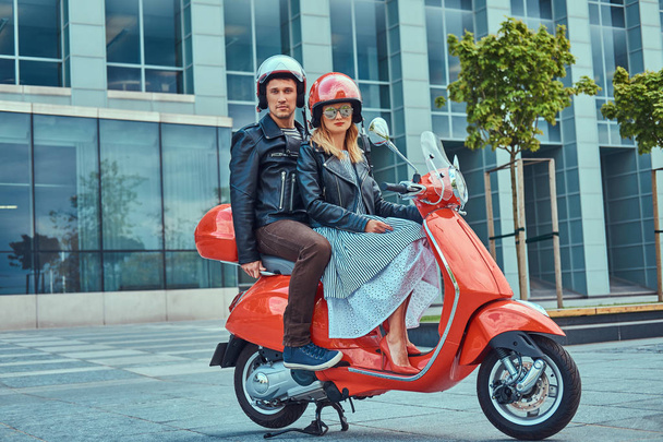 Coppia attraente, un bell'uomo e una donna sexy che cavalcano insieme su uno scooter rosso retrò in una città
. - Foto, immagini