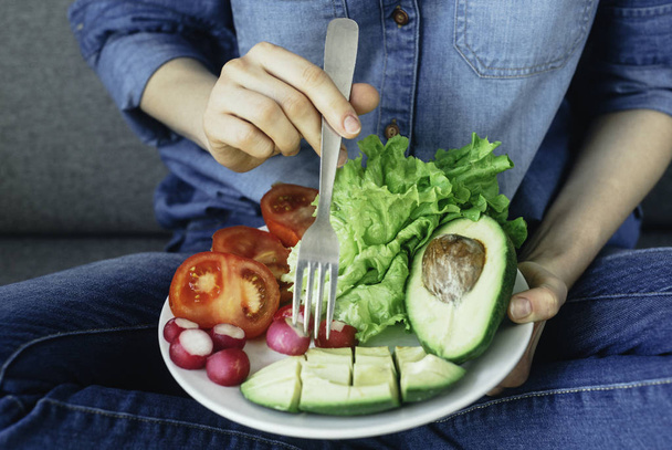 junge Frau isst zu Hause frisches Gemüse. Vegane Ernährung von Avocad - Foto, Bild