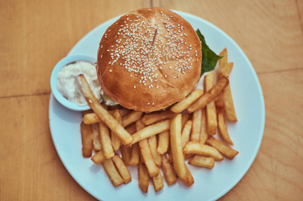 Κοντινό πλάνο εικόνα ένα χάμπουργκερ με πατάτες τηγανητές και πικάντικη σάλτσα με ένα λευκό πιάτο. Έννοια των ανθυγιεινών τροφίμων. - Φωτογραφία, εικόνα