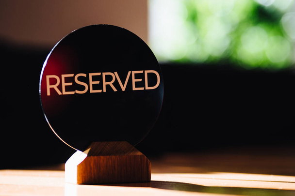 Wooden reserved sign with capital letters on dining restaurant table. Table reservation concept. Reserved banner. Blurred background. Nobody in photo. - Foto, Bild