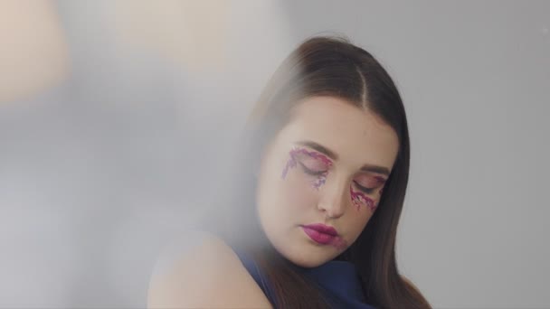 Młody model z Recenzje makijaż w odcieniach purpurowym w studio strzelać - Materiał filmowy, wideo