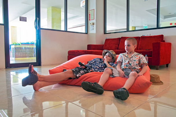 Δύο αγόρια (8-10 ετών) να κάθονται στο μαξιλάρια δαπέδου και παρακολουθήσετε τηλεόραση πρόσοψη. - Φωτογραφία, εικόνα