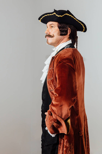 mustachioed eccentric man in the vintage clothes of the baron. Hat tricorn, brown jacket. - Zdjęcie, obraz