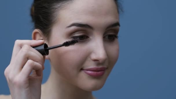 Young woman applying mascara on her lashes and smiling, make-up concept - Video