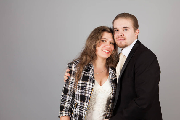Elegant couple smiling for the camera while embracing. On grey background. - Foto, Bild