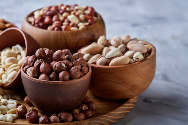 Mixed nuts in brown bowls on wooden tray over white background, close-up, top view, selective focus. - Photo, image