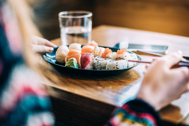 Καλλιέργεια γυναίκα τρώει σούσι σε φόντο - Φωτογραφία, εικόνα