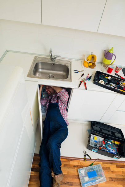 Hombre adulto acostado en el piso de reparación de fregadero en la cocina
 - Foto, Imagen