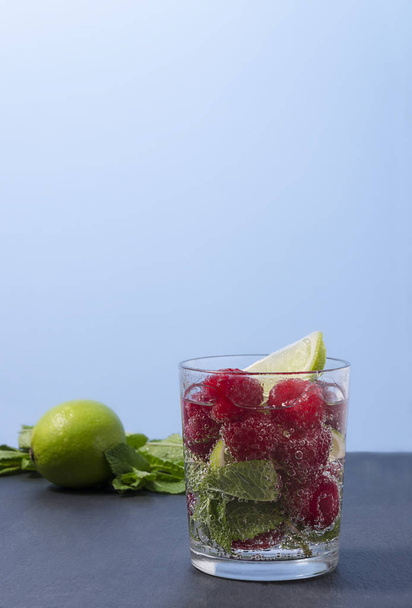 Raspberry lemonade with lime and mint in a glass. Non-alcoholic raspberry refreshment drink. Raspberry mojito in a glass with mint and lime. - Фото, зображення