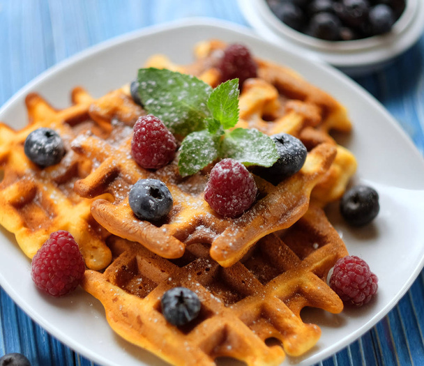 Traditional belgian waffles with fresh berrys and sugar powder on white plate, blue wooden background. Flat lay, top view, copy space. - 写真・画像