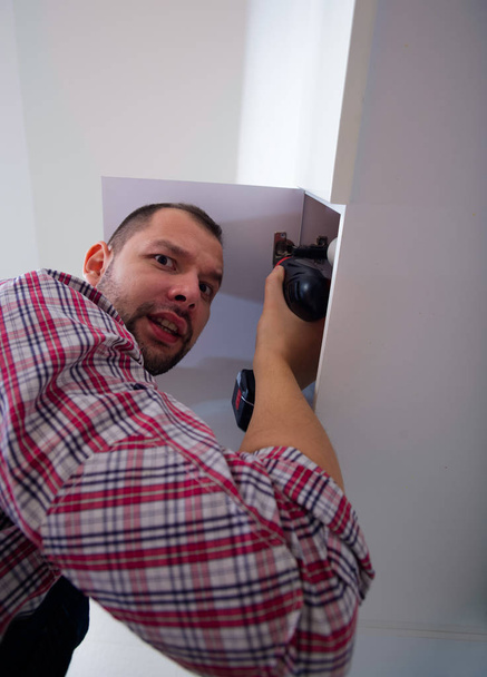 Adult guy repair door on the cabinet in the kitchen - Photo, Image