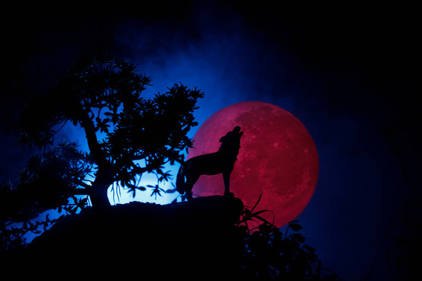 Silueta de lobo aullando contra fondo de niebla tonificado oscuro y luna llena o lobo en silueta aullando a la luna llena. Halloween concepto de horror
. - Foto, imagen