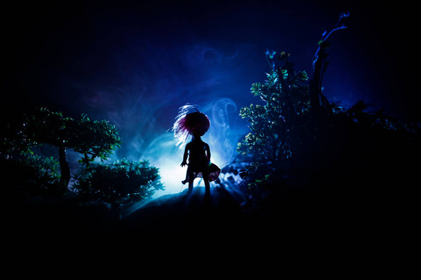 Horror Halloween utrzymane obraz koncepcyjny. Sama dziewczyna z światło w lesie w nocy. Sylwetka dziewczynę stojącą między drzewami z surrealistyczne światło. Selektywny fokus. - Zdjęcie, obraz