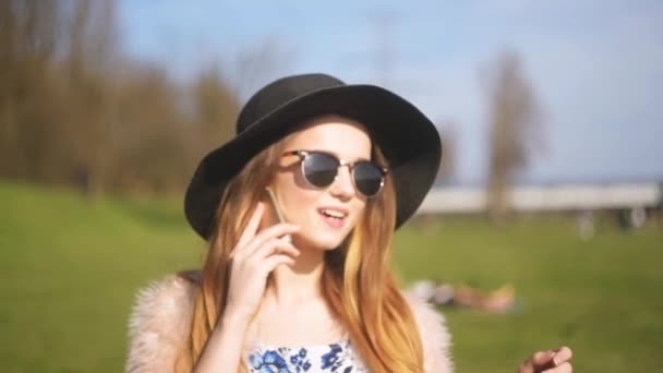 Siyah bir şapka ve güneş gözlüğü güzel bir kız sokakta telefonda konuşuyor. Gezi çağrıları, mutlu ve gülümseyen kız. Gezici kavramı. - Video, Çekim