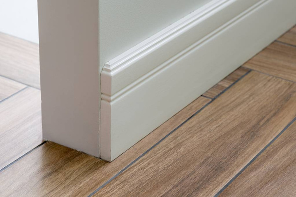 Moulding in the corner. Light matte wall with tiles immitating hardwood flooring - Photo, Image