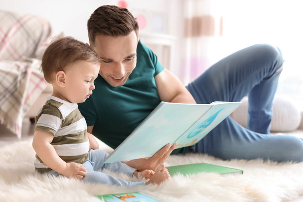 Junger Vater liest Buch mit seinem süßen kleinen Sohn zu Hause - Foto, Bild