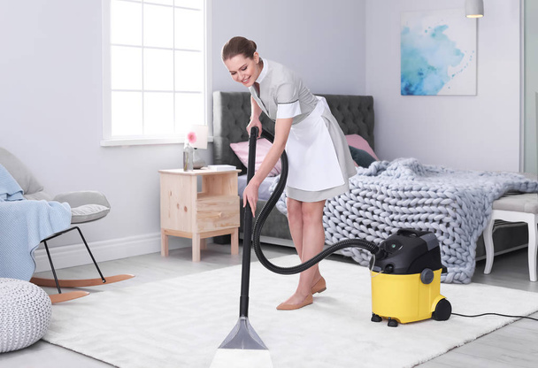 Young woman hoovering carpet with vacuum cleaner in bedroom - Valokuva, kuva