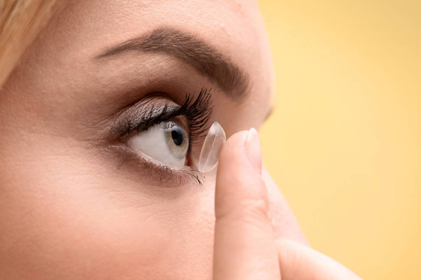 Young woman putting contact lens in her eye on color background, closeup - Foto, afbeelding