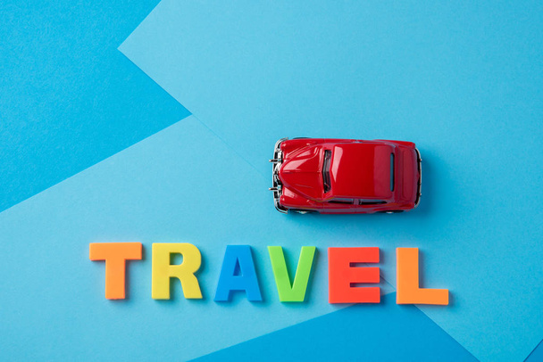 Red toy car and inscription plastic travel letters on a blue bac - Photo, Image