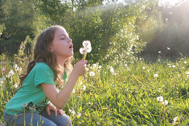 Adolescente soplando semillas de una flor de diente de león en un parque de primavera
 - Foto, Imagen