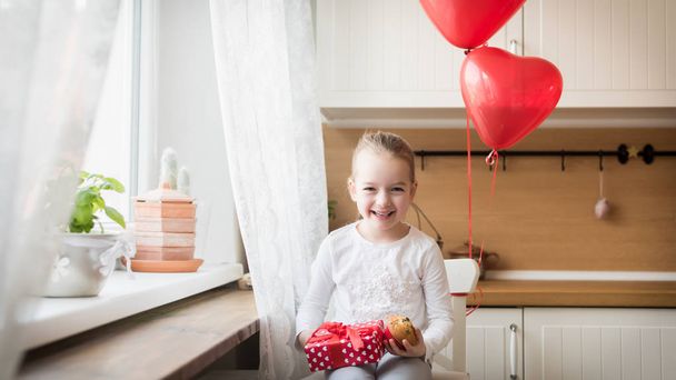 Cute preschooler girl celebrating 6th birthday. Girl holding her birthday cupcake and beautifully wrapped present, surrounded by balloons. - Fotoğraf, Görsel