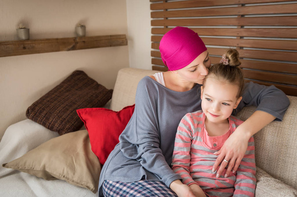 Młody dorosły kobieta rak pacjent spędzać czas z córką w domu na kanapie. Raka i koncepcja wsparcia rodziny. - Zdjęcie, obraz