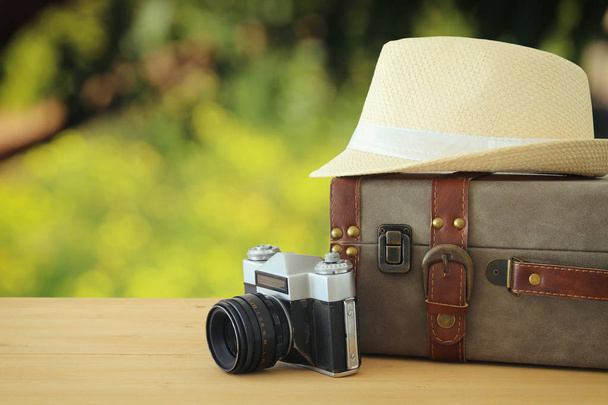 equipaje vintage viajero, cámara y sombrero fedora sobre mesa de madera frente al paisaje bokeh. vacaciones y concepto de vacaciones
. - Foto, Imagen
