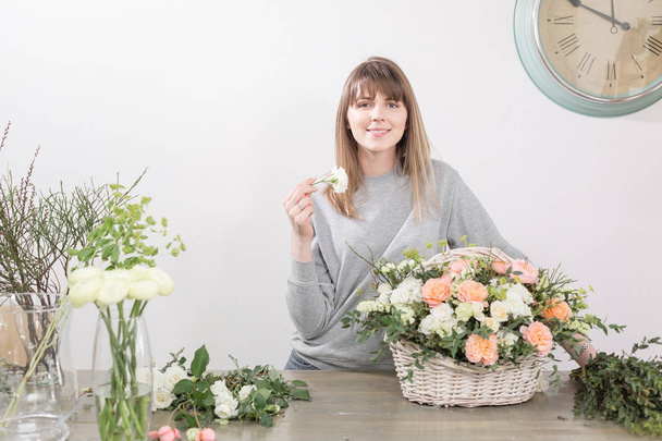 lächelnde Floristin. Blumenwerkstatt - Frau, die eine schöne Blumenkomposition zu einem Strauß in einem Weidenkorb macht. Floristikkonzept - Foto, Bild