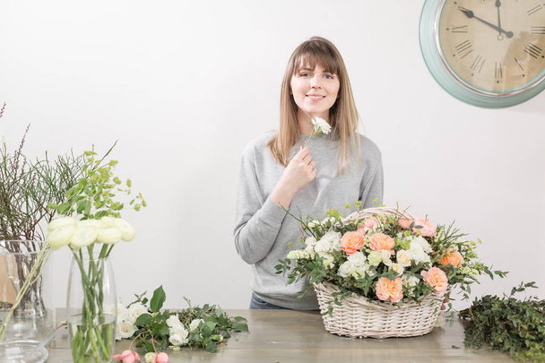 lächelnde Floristin. Blumenwerkstatt - Frau, die eine schöne Blumenkomposition zu einem Strauß in einem Weidenkorb macht. Floristikkonzept - Foto, Bild