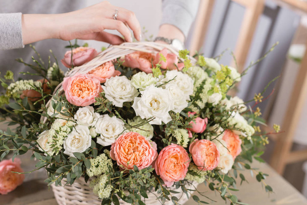 close-up hands female florist. Floral workshop - woman making a beautiful flower composition a bouquet in a wicker basket. Floristry concept - 写真・画像