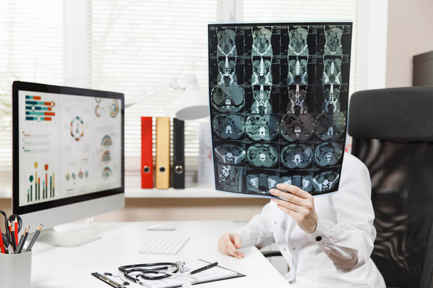 Femme médecin assis au bureau avec ordinateur, film radiographie du cerveau par l'image radiographique ct scanner mri dans le bureau de la lumière à l'hôpital. Femme en robe médicale dans la salle de consultation. Santé, concept de médecine
. - Photo, image
