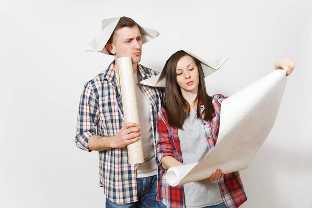 Young concerned woman, man in casual clothes holding unrolled wallpaper rolls. Couple isolated on white background. Instruments, accessories, tools for renovation apartment room. Repair home concept. - Photo, image