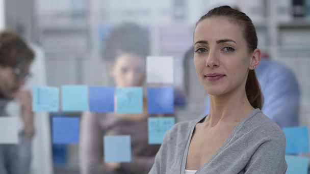 Jeune femme souriante posant dans le bureau et l'équipe d'affaires travaillant sur le fond
 - Séquence, vidéo