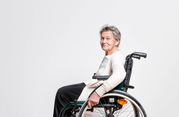 Portrait of a senior woman with wheelchair in studio. - Φωτογραφία, εικόνα