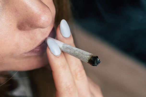 Kobieta pali cannabis weed, wspólne i lżejsze w jego ręce. Pali na czarnym tle. Pojęcia dotyczące używania marihuany i legalizacji konopi. - Zdjęcie, obraz