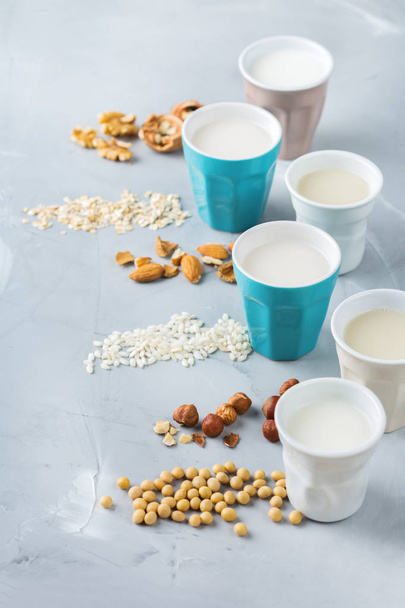 Food and drink, health care, diet and nutrition concept. Assortment of organic vegan non diary milk from nuts, oatmeal, rice, soy in glasses on a kitchen table - Фото, изображение