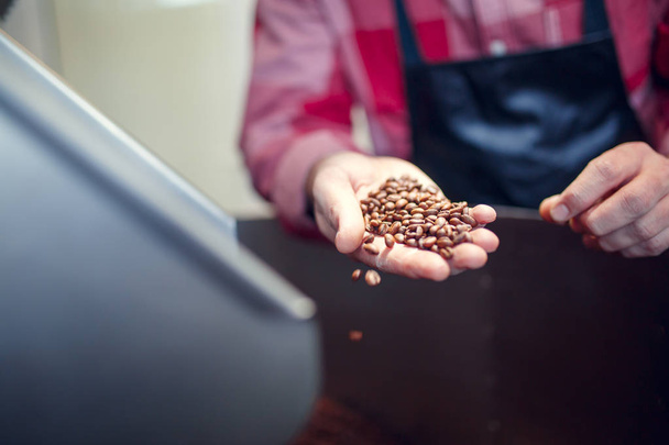 Photo of young businessman holding roasted coffee beans near industrial coffee grinder - Φωτογραφία, εικόνα