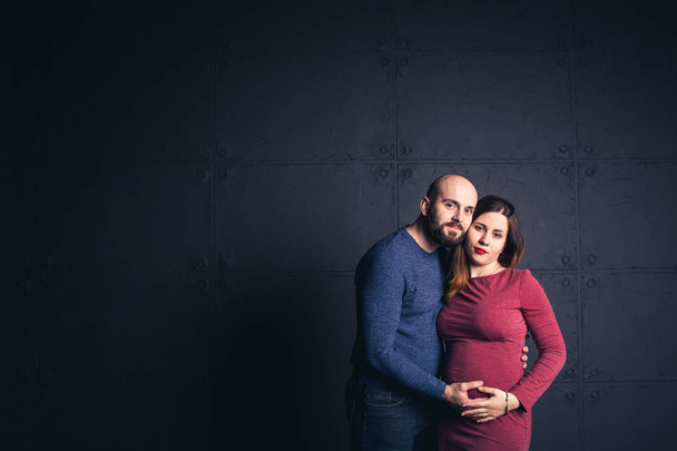 bearded man holding belly of pregnant woman in studio on dark background. Copy space. - 写真・画像