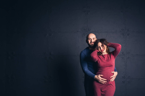 γενειοφόρο άτομο που κρατά το στομάχι και έγκυος γυναίκα αγγίζει τα μαλλιά, στο studio σε σκούρο φόντο. Χώρο αντίγραφο. - Φωτογραφία, εικόνα