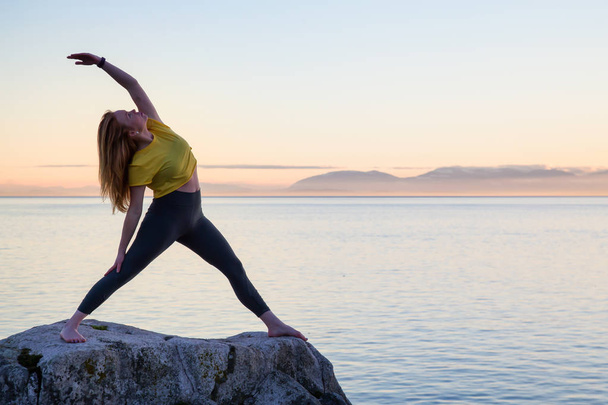 Young woman practicing yoga on a rocky island during a vibrant sunset. Taken in Whytecliff Park, Horseshoe Bay, West Vancouver, British Columbia, Canada. - Foto, Imagem
