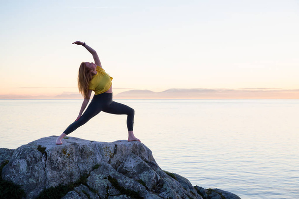 Young woman practicing yoga on a rocky island during a vibrant sunset. Taken in Whytecliff Park, Horseshoe Bay, West Vancouver, British Columbia, Canada. - Fotoğraf, Görsel