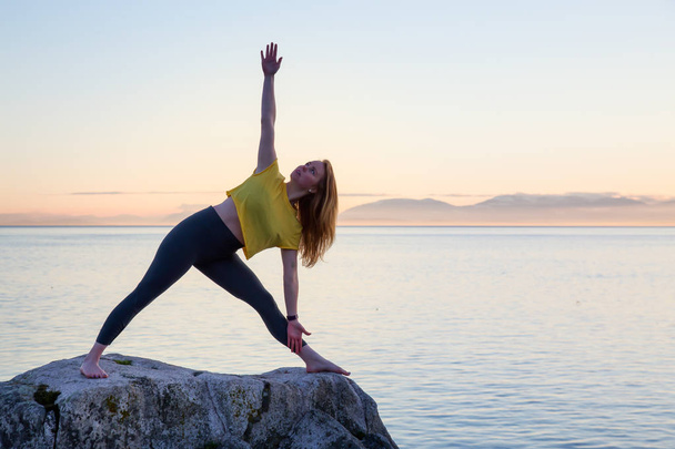 Young woman practicing yoga on a rocky island during a vibrant sunset. Taken in Whytecliff Park, Horseshoe Bay, West Vancouver, British Columbia, Canada. - 写真・画像
