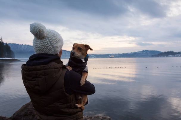 Young woman holding her little dog, Chihuahua, in her arms during a vibrant sunset. Taken in Belcarra, Vancouver, British Columbia, Canada. - Photo, image