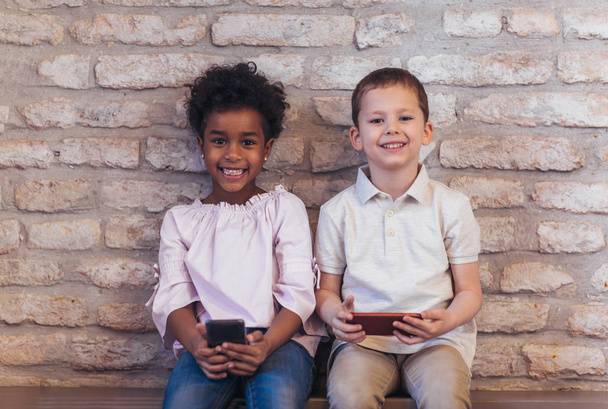 Ποικιλομορφία παιδιά φίλων χρησιμοποιώντας ψηφιακές συσκευές έννοια, τούβλο τοίχο πλαίσιο. - Φωτογραφία, εικόνα