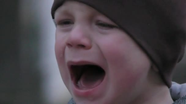 Kind jongen huilen. Close-up, twee jaar oud kind in een hoed huilen in de straat. Het kind weigert de snoep. - Video